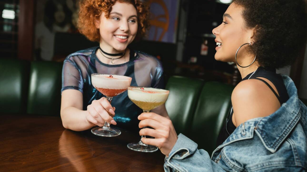 Cheerful interracial friends holding clover club and pisco sour cocktails in bar