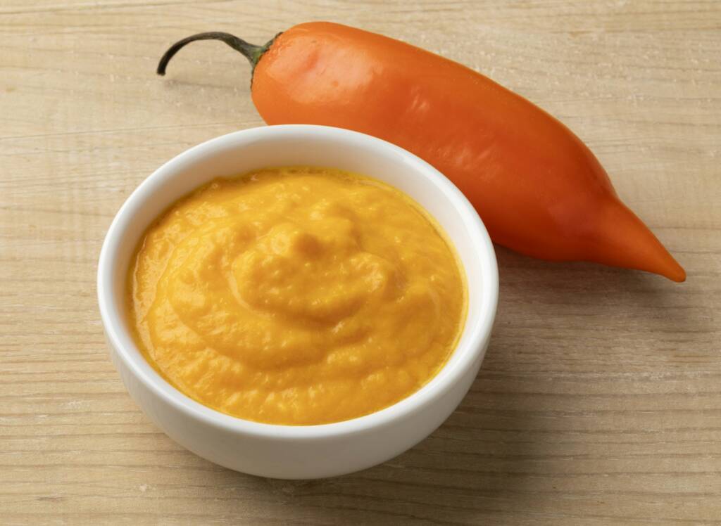 Fresh Peruvian Aji Amararillo pepper and a bowl with Aji Amarillo sauce close up