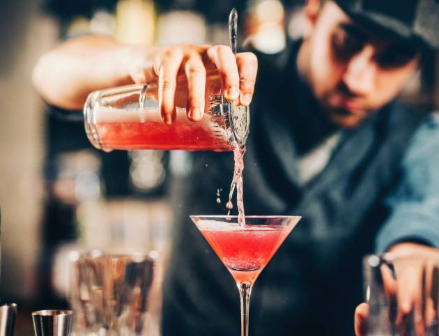 barman preparing and pouring red cocktail in martini class.